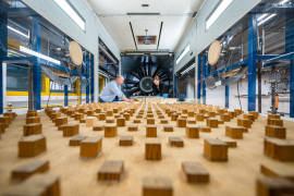 Vorbereitung eines Windkanalmodells im Bochumer Grenzschichtwindkanal mit Blick in Strömungrichtung: Im Hintergrund ist das Sauggebläse zu sehen, die Holzkuben im Vordergrund sind Rauigkeitskörper, die zur Ausbildung einer turbulenten Strömungsgrenzschicht beitragen, die in kleinem Maßstab einen Starkwind in der Natur nachbildet. (Foto © Damian Gorczany) 