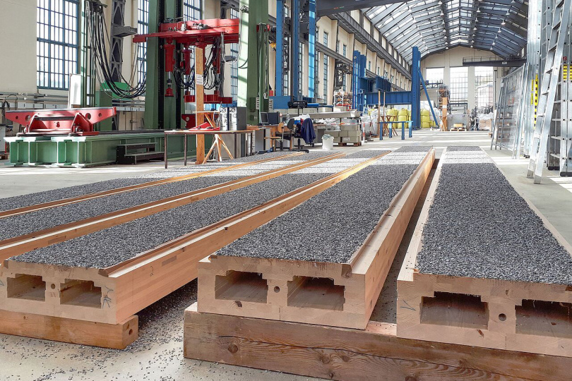 In der Peter-Behrens-Halle, der Versuchshalle der Bauingenieure der TU Berlin, wurde der neue Holz-Beton-Verbund erforscht. Bei dem Verfahren werden Holz und Beton miteinander verklebt. Im Vordergrund sieht man Holzelemente, auf die ein Granulatsplitt aufgetragen wurde. Darauf wird der Beton gegossen. Es entsteht eine sehr tragfähige Verbindung. © TU Berlin/Fachgebiet Entwerfen und Konstruieren, Verbundstrukturen 