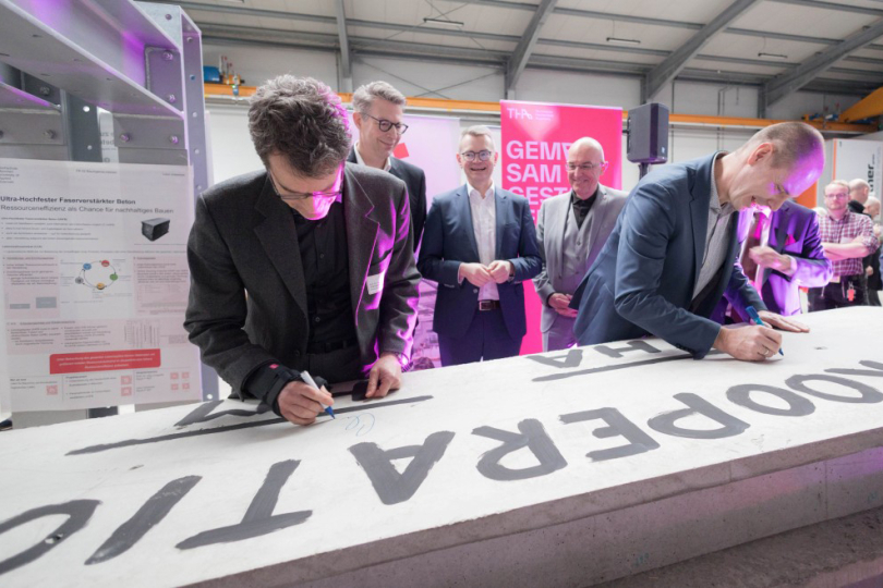 Bei der offiziellen Eröffnung des Technologietransferzentrums Aichach durch den Bayerischen Wissenschaftsminister Markus Blume, MdL (2.v.l.) unterschrieben Prof. Dr. Frank Danzinger, Vizepräsident für Technologie und Forschung der THA (rechts) und Prof. Dr.-Ing. Christian Seiler, Dekan an der Fakultät Bauingenieurwesen der Hochschule München (links) , die gemeinsame Kooperationsvereinbarung – symbolisch auf einer querschnittsoptimierten Carbon-Betonplatte für Gebäude, die am TTZ Aichach entwickelt wird (Foto: Matthias Leo/THA) 